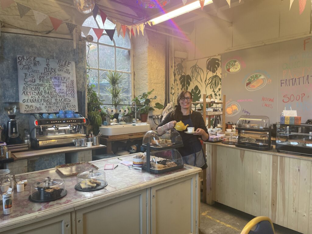 A member of the Unity Yard team posing with a cup of coffee by the till in the Unity Yard Café