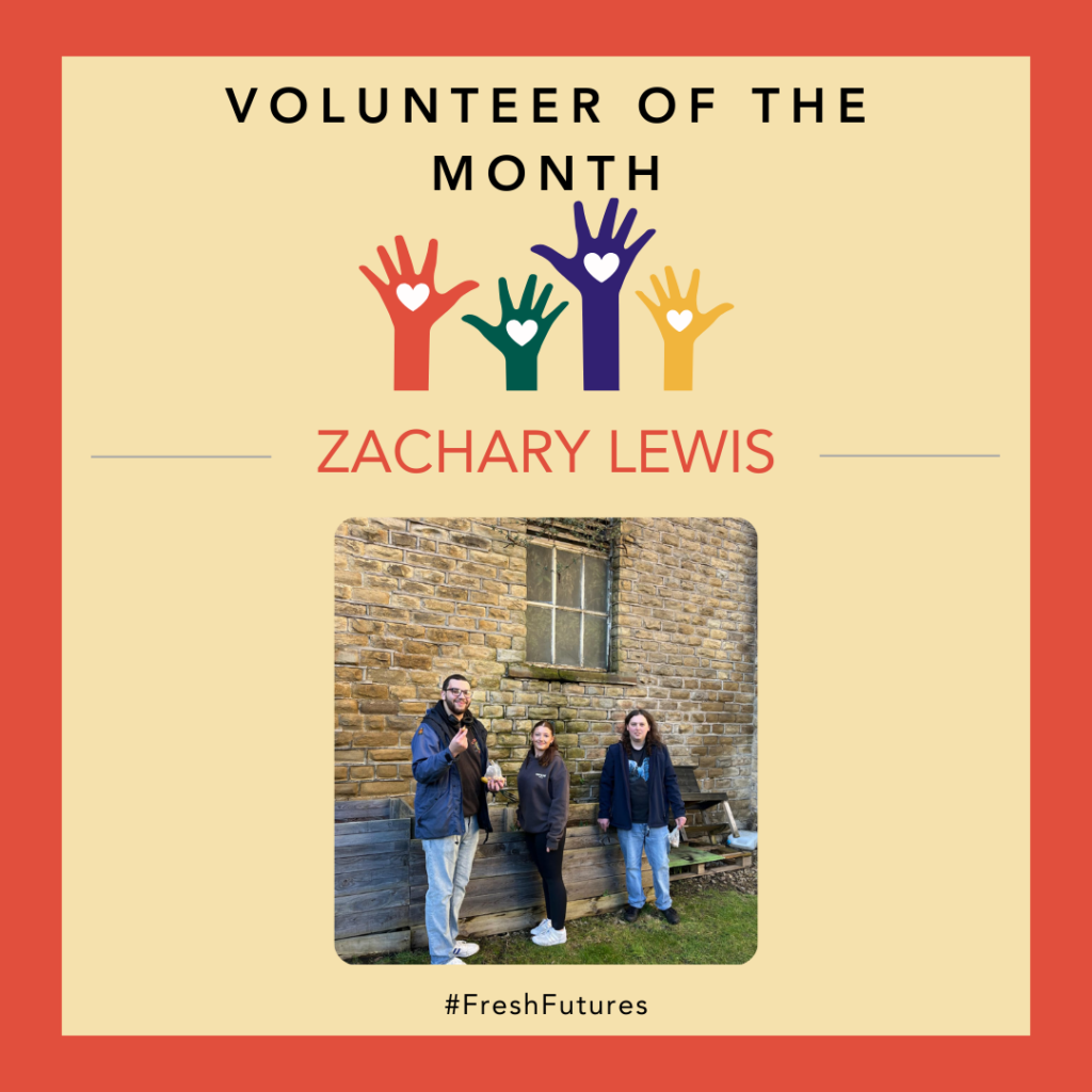 A poster that says Volunteer of the Month at the top, with some hands reaching up below the title. Under these is a picture of 3 people stood next to a building looking at the camera.