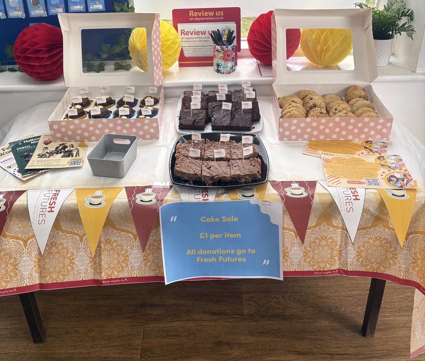 An image of cookies, and sweet treats on a table decorated with Fresh Futures bunting and a sign saying 'Cake Sale, £1 per item'. 